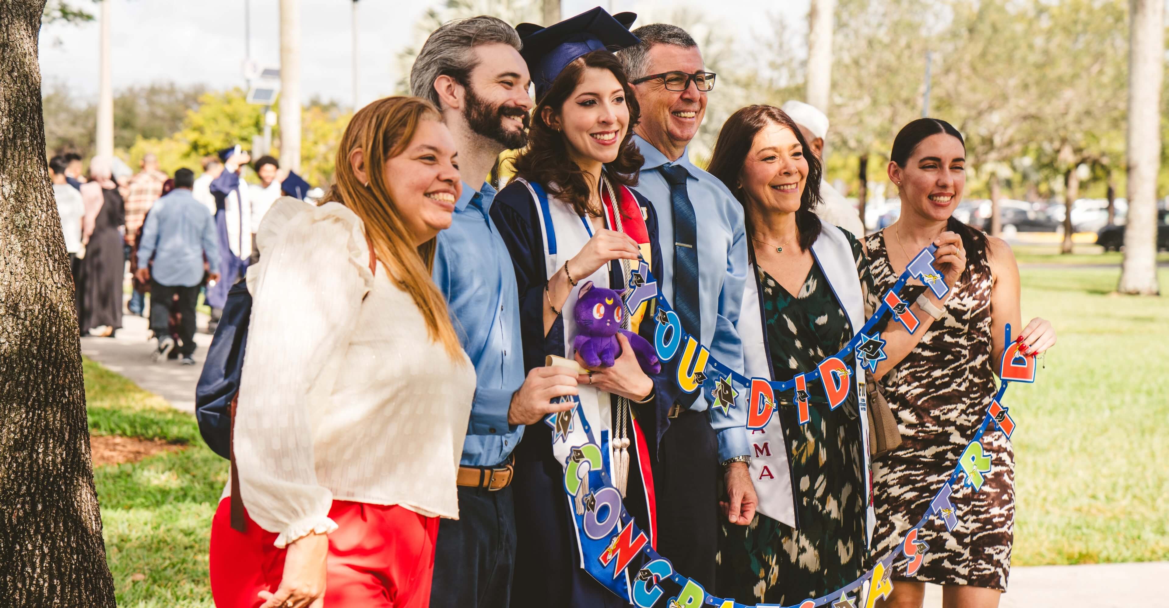 Graduate posing outdoors with her family holding congratulations banner